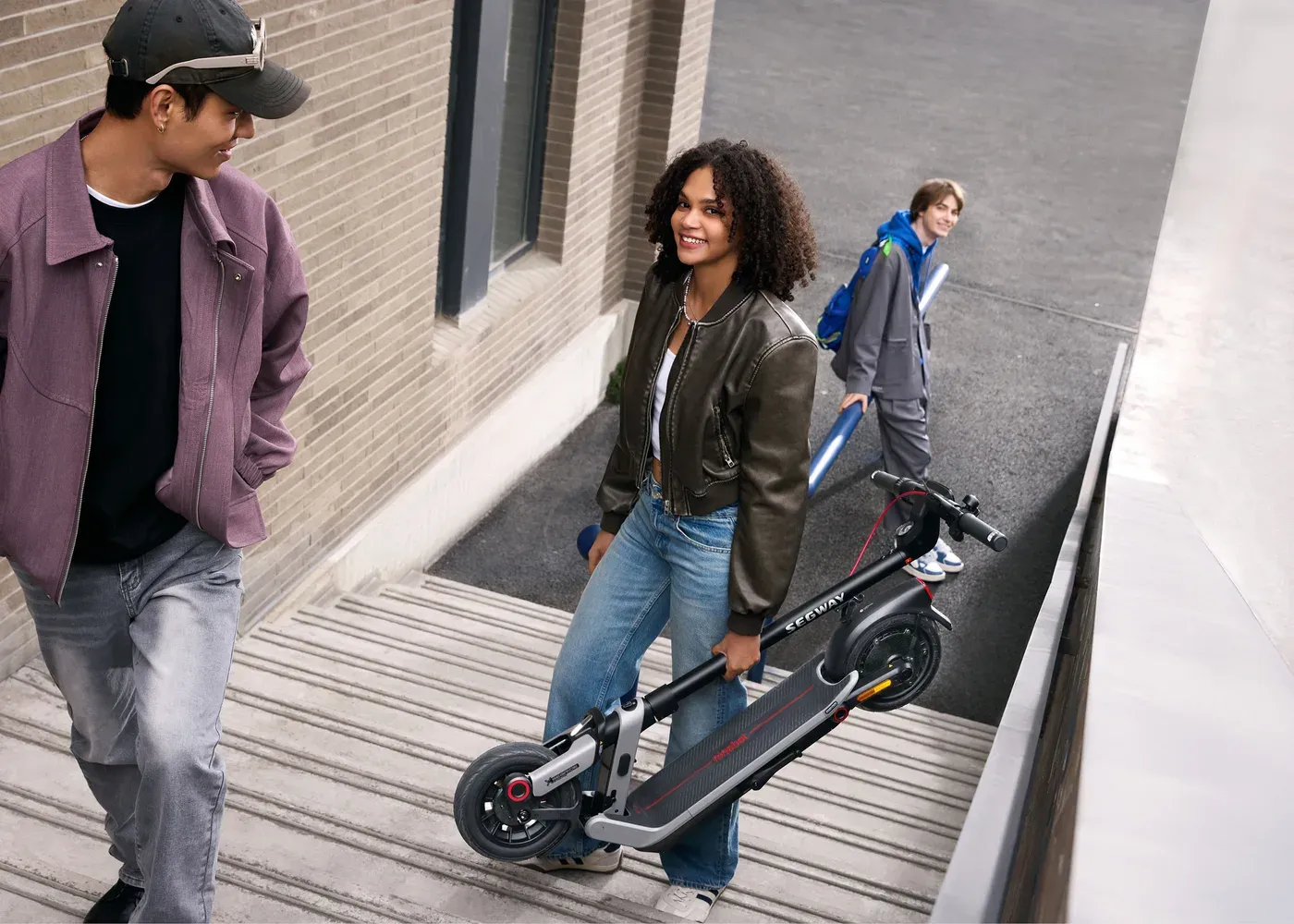 Une jeune femme monte un escalier extérieur en portant une Ninebot E3 Pro E pliée à la main